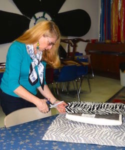 Ellen Ciompi, President of the Board of The Scrap Exchange, our partner in the Musical Chairs fundraiser, cuts fabric for the seat of the “Chair-lo” (cello chair) created by woodcrafter Edmund Daugherty.